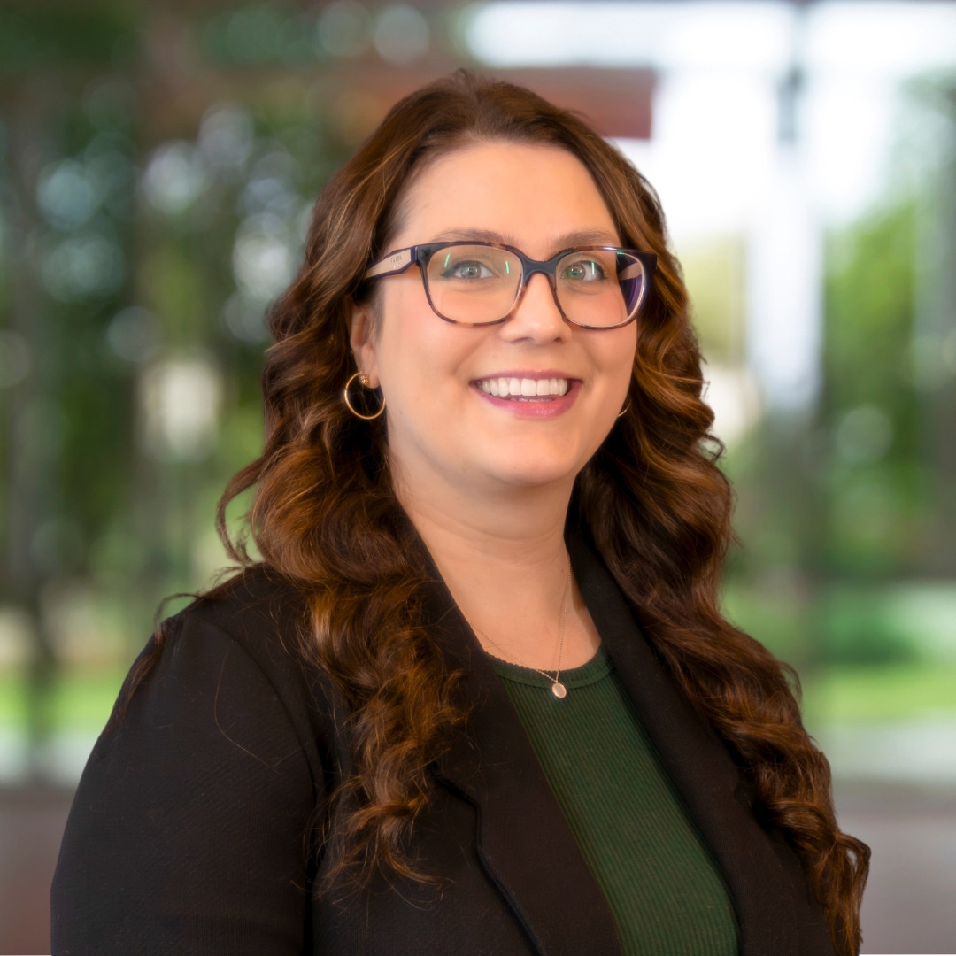 Headshot of Lisa Lorentz, a smiling woman with long brown hair, glasses, a dark blazer, and a green top.